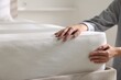 © New Africa - Woman touching soft mattress on bed indoors, closeup