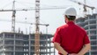 © Deamard - Engineer in a white helmet looking at a large construction site with cranes.