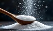 © Md - White sugar or salt granules being scooped with a wooden spoon with falling particles on a dark background