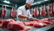 © Pete - Man in chef uniform with gloves cuts raw red meat on steel table. Carcasses hang behind in butcher shop cooler. Fresh beef steaks prepared for sale or cooking. Quality butcher shop.
