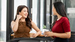 © NAMPIX - Two happy Asian businesswomen talking and drinking coffee during a break in a modern office or cafe.