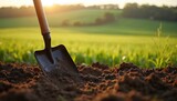 Shovel rests in rich brown earth. Endless green fields stretch to the horizon under warm sun. Farming tool symbolizes hard work, cultivation, and connection to land.