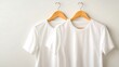 © Tanvir - Two plain white t-shirts hanging on wooden hangers against a light background, showcasing simplicity and versatile fashion.