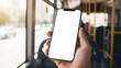 © MD Rashedul Islam - Hand holding mobile phone with blank white screen mockup in public transport bus interior with city street sun flare background for app presentation travel website digital copy space.