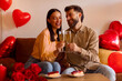 © Home-stock - Happy man and woman raising their glasses in toast, having romantic dinner, celebrating anniversary or Valentines day, sitting on sofa with red balloons around