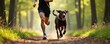 © Maryna - Man and dog run on forest trail during daytime. Fit person wears black sportswear. Animal has harness, leash connects to owner. They compete in outdoor race, enjoy healthy activity together.