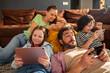 © Geber86 - Happy adult parents and children playing on smartphones and tablet in living room