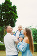 © DSMT - Family enjoys time in park with child during warm afternoon while trees sway gently in the background under partly cloudy sky