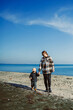 © DSMT - Mother and child walk on beach shoreline under clear sky near calm ocean water during daylight hours