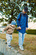 © DSMT - Mother helps child walk along a low wall in a grassy area during daylight hours