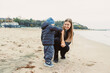 © DSMT - Child and adult enjoy a day at the beach in the afternoon, collecting seashells on a sandy shore while the sun sets in the background over the water and trees