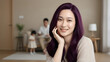 © satrio - A smiling woman with vibrant purple hair in a cozy home setting with family in the background.