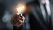 © sablengjago - A person in a suit is holding up a glowing light bulb, representing a new idea or inspiration. The background is blurred