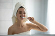 © fizkes - Healthy morning habits. Head shot portrait happy young lady with perfect smile wrapped in towels after shower clean teeth with fluoride minty toothpaste flexible brush look at wall mirror in bathroom