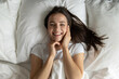 © fizkes - Good sleep for natural beauty. Top view portrait pretty cheerful young woman lie in large comfortable bed wake up after sweet night dreams look at camera caress face celebrate healthy refreshed skin