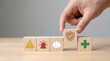 © CuteBee - A hand carefully selects a block representing safety and security focusing on health protection and hazard awareness from a row of wooden cubes