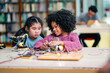 © Wanwajee - Black girl collaborates with Asian girl during robotics learning session, connecting wires, assembling robot parts, STEM education focus, diversity, teamwork skills, technology curiosity in classroom.
