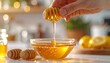 © Rina - Hand Drizzling Golden Honey From Wooden Dipper Into Glass Bowl With Lemons And Honey Jars In Blurred Kitchen Background Soft Sunlight