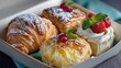 ©  VladaToday - Assorted holiday pastries in box with mini tarts, croissants, and whipped cream toppers