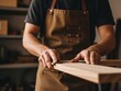 © Mst Muslima - A person wearing a brown apron working with a piece of wood in a workshop setting with tools and shelves in the background