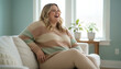 © Iryna - Caucasian plus size woman laughing on sofa in cozy living room, body positivity and joyful lifestyle in relaxed home environment