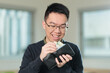 © fotolite - A smiling Chinese student wearing glasses removes cash bills from his wallet, perfect for student finance, money management, or personal budgeting concepts.