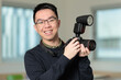 © fotolite - A happy Chinese student holds a professional camera with external flash unit mounted on top, perfect for photography education, film school, or media arts concepts.