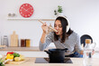 © Xavier Lorenzo - Happy young beautiful housewife tasting food with wooden spoon while listening music with headphones in the kitchen at home