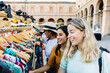 © Xavier Lorenzo - Multiracial young female friends choosing clothes outdoors. Cheerful women enjoying shopping time during a city trip. Lifestyle and travel concept.