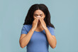 © Prostock-studio - Young african american woman touching her nose bridge, suffering from rhinitis, seasonal allergy or antritis, standing over blue background, studio shot.