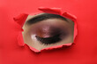 © New Africa - Young woman with evening makeup, closeup. View on eye through torn hole in red paper
