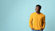 © Prostock-studio - Happy millennial black man in casual outfit holding hands in pockets, looking at copy space for text or advertisement and smiling, recommending nice offer or discounts, studio shot on blue, panorama