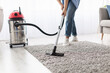 © Prostock-studio - Closeup cropped low section of unrecognizable young casual woman using vacuum cleaner washing gray rug floor carpet in living room or bedroom. Chores Concept. Blurred Background, Free Copy Space