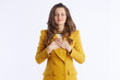 © Alliance - A professional woman in a mustard blazer finds a serene moment, with hands on her chest and eyes closed, embodying gratitude, contentment, or self-care in a busy life.