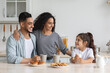 © Prostock-studio - Happy arabic family having breakfast while spending weekend together at home, cheerful young father, mother and curly little girl sitting at kitchen, drinking coffee and milk with homemade cookies