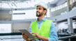 © Prostock-studio - A construction worker stands inside a building site wearing a hard hat and safety vest. He looks at a tablet as he manages tasks and checks information.