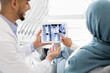 © Prostock-studio - Middle eastern dentist showing xray of teeth treatment process on digital tablet to islamic female patient during check up in modern dental clinic, muslim lady in hijab pointing at tab computer