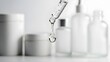© lepiangg - Close-up of a cosmetic dropper dispensing a clear liquid drop, with blurry white skincare product containers in the background, suggesting beauty and wellness routines for healthy skin