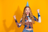 Young woman celebrates birthday with party hat and tie dye top against yellow background