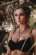 © blackday - Close-up portrait of confident woman wearing black lace lingerie among tropical palm leaves