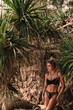 © blackday - Stylish woman wearing black lace lingerie poses on rocky tropical beach surrounded by palm trees