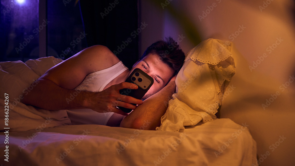 Man reading smartphone messages while lying on pillow. Concept of mobile communication, messaging apps, digital interaction, real time connectivity, smartphone technology, online services.