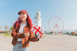 © EdNurg - Smiling woman with pink hair standing outdoors, holding Georgian flag with Batumi lighthouse and Ferris wheel in background