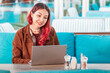 © EdNurg - Woman sitting at a modern cafe, typing on a laptop, enjoying remote work and digital lifestyle