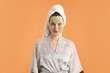 © New Africa - Beautiful woman with cosmetic mask on face and hair wrapped in towel against orange background
