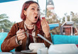 © EdNurg - Young woman tasting hot soup in an outdoor restaurant, showing a funny reaction with her hand near her mouth