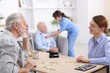 © New Africa - Woman playing dominoes with senior man at table and care worker helping her patient at retirement home, selective focus