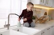 © New Africa - Child safety at home. Little boy pulling down faucet hose on counter in kitchen