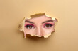 © New Africa - Young woman with beautiful makeup, closeup. View on eyes through torn hole in beige paper