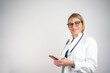 © Nenad - Woman doctor posing isolated over grey wall background using mobile phone.